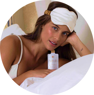 Woman in bed with a white headband, holding a pouch of N2B4B Glow Fuel Liquid Collagen